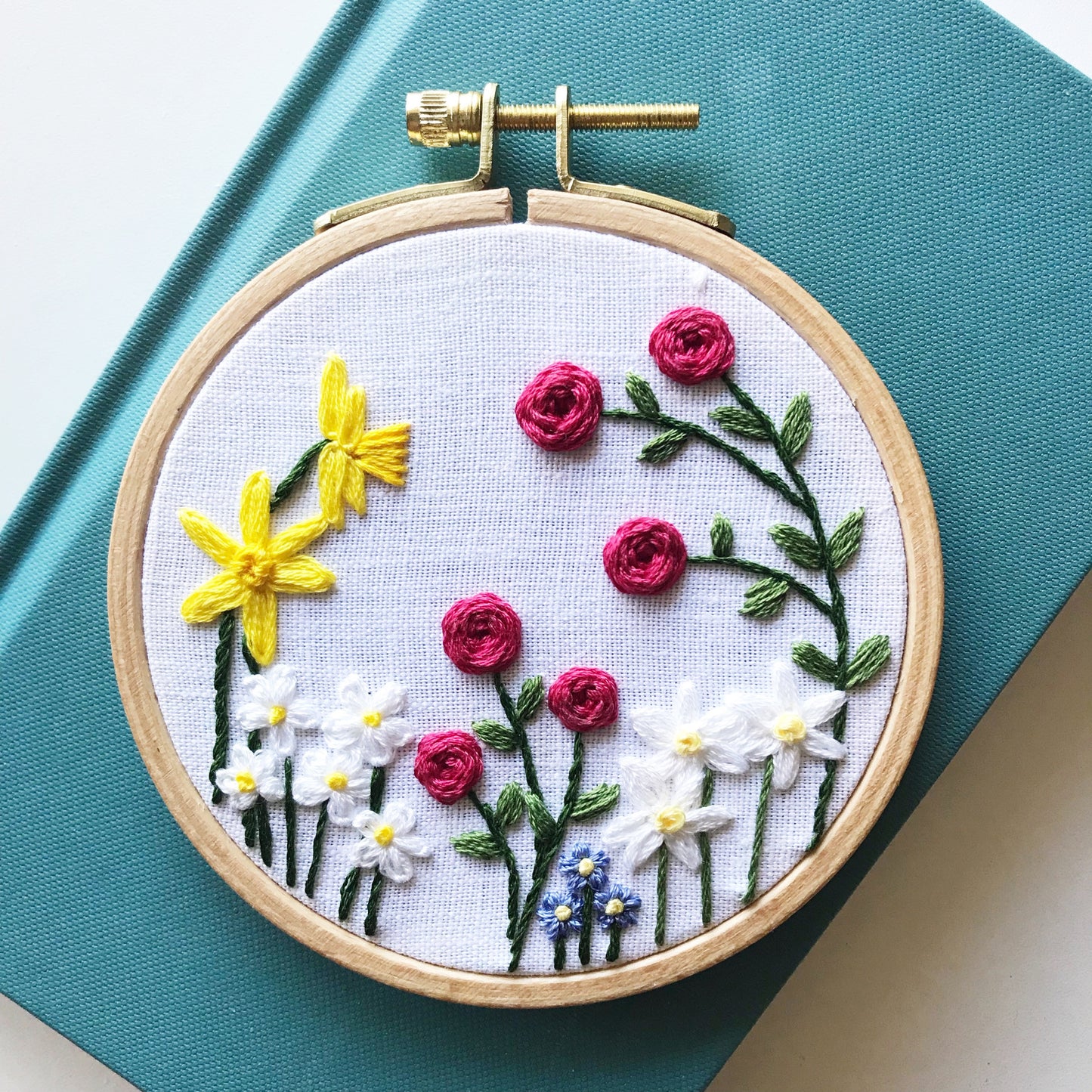 Choose your own adventure for your flower garden. Hoop shows Roses, Daisy, daffodils, paper whites and forget me nots on a white linen background.