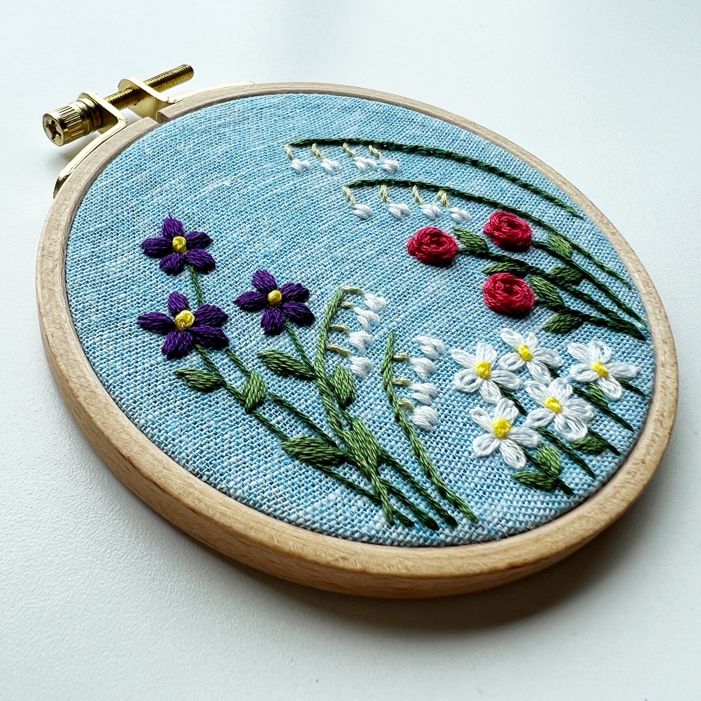 Choose your own adventure for your flower garden. Hoop shows Lily of the Valley, Roses, Daisy and violets on a blue background.
