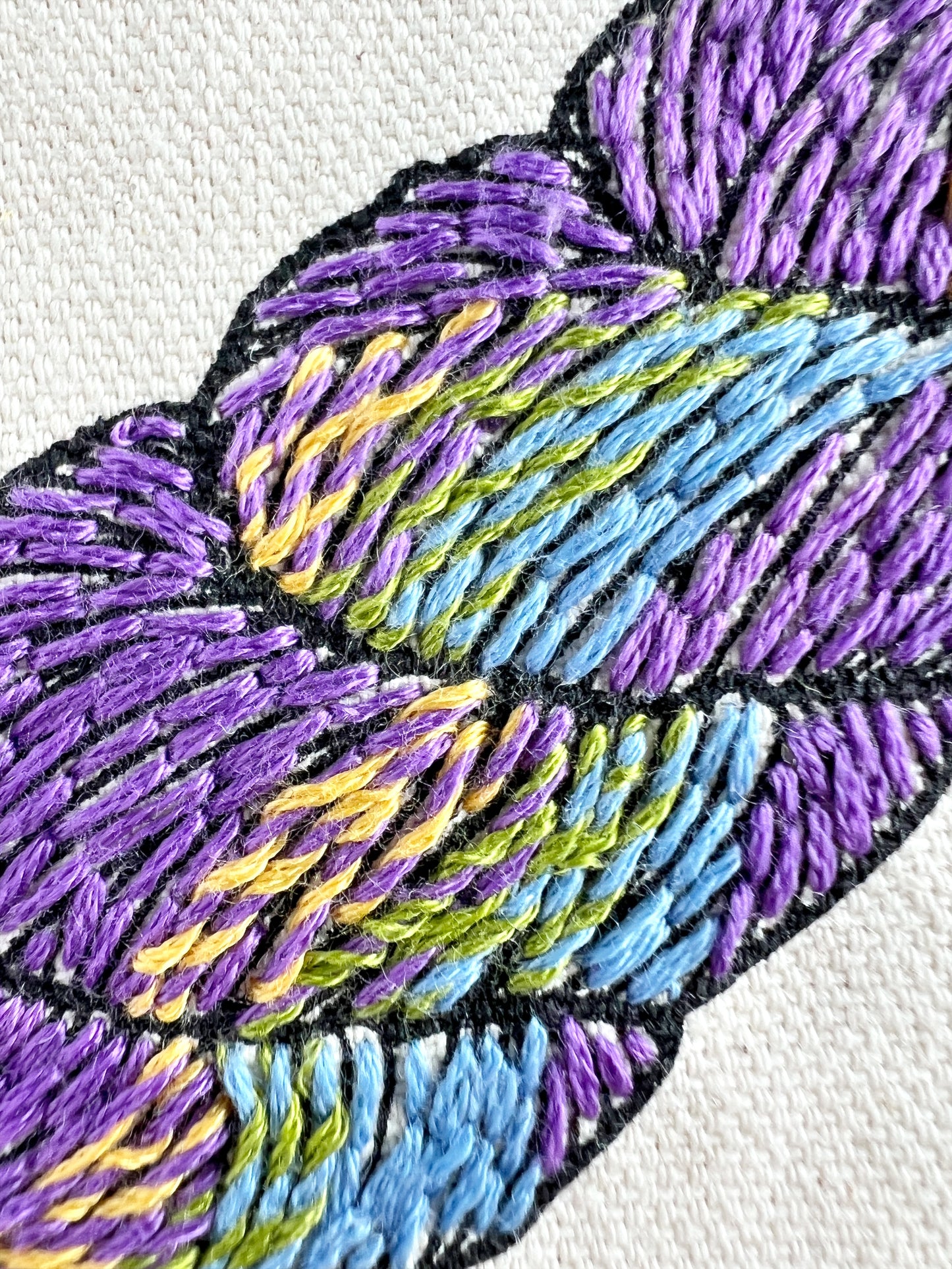 Close up of stitching on Fiber Fluid Tote. Skein of yarn is embroidered in purple, teal, green and yellow to evoke a variegated yarn.
