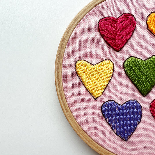 Close up of I Heart Stitching Complete Beginner Embroidery Kit.  Hearts in red, yellow, green, and purple show four different stitch types.