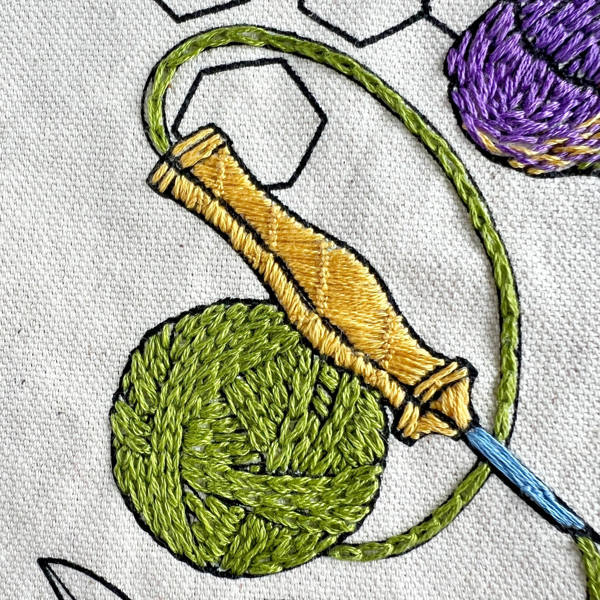 Close up of punch needle and green yarn on Rosanna Diggs Fiber Fluid Tote.  Wraps of the yarn ball are highlighted by changing stitch direction.  Punch Needle has blue tip and detailed handle in yellow gold floss.