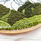 Up close photo of Hurricane Ridge Embroidery.  Stitch details in green highlight trees, hills and grass.  Mountain can be seen in the background.