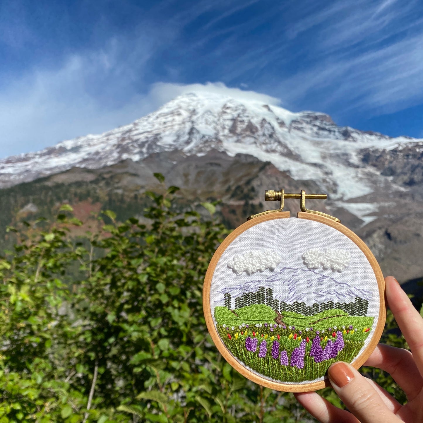 Completed Mount Rainier embroidery held in front of Mount Rainer in Washington state.