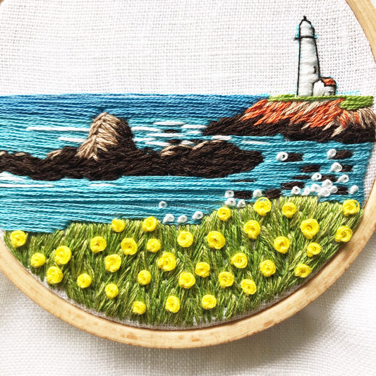 Lighthouse by the Bay PDF. Download includes easy to follow directions.  Hand Embroidery has lighthouse on the right hand side on cliff with rocks and ocean to the horizon.  Grass and flowers fill the foreground.